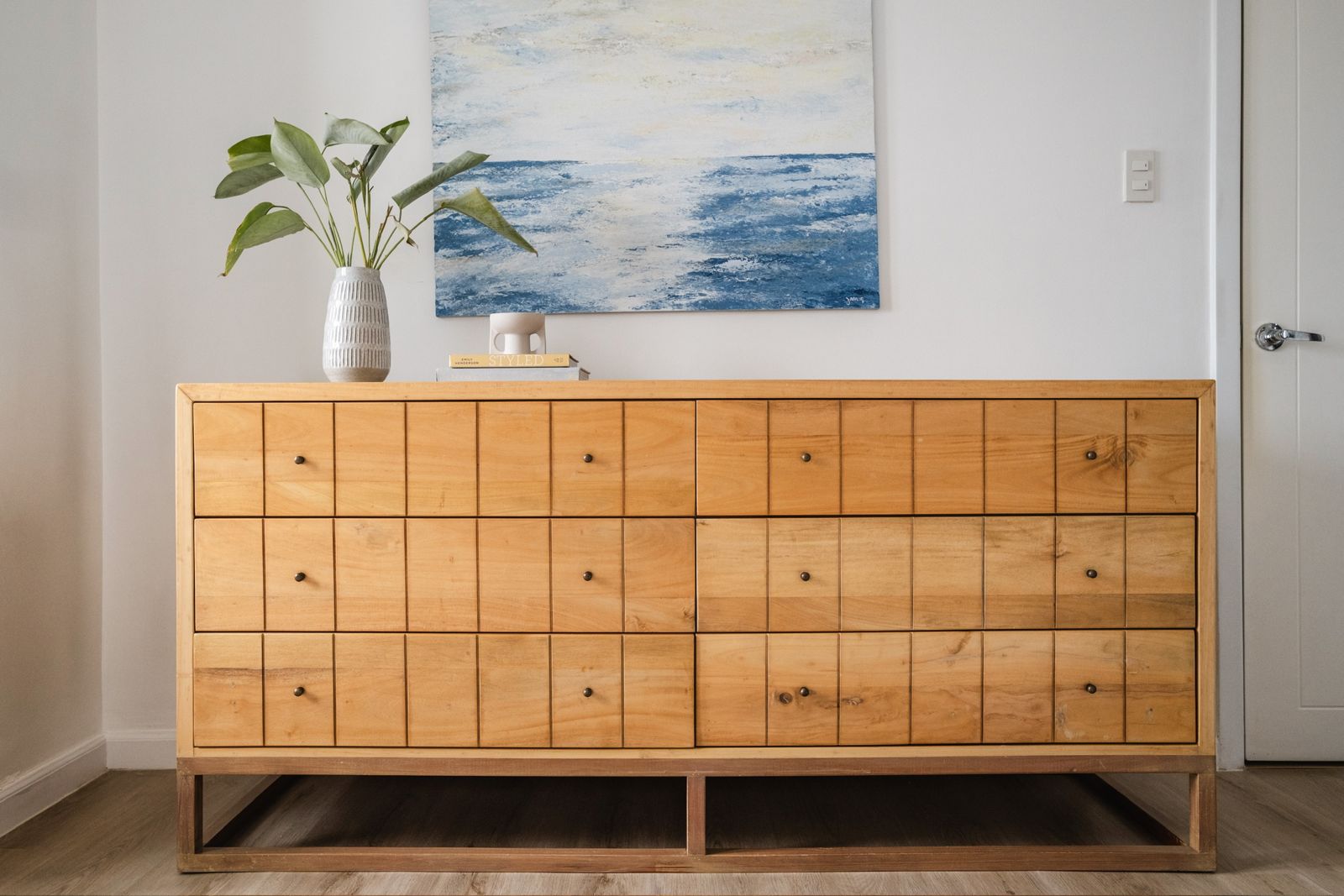 Natural-wood dresser with grid-front drawers in a bright condominium bedroom.