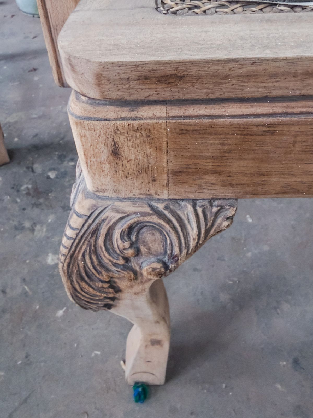 Close-up of an ornate carved wooden chair leg during surface preparation.