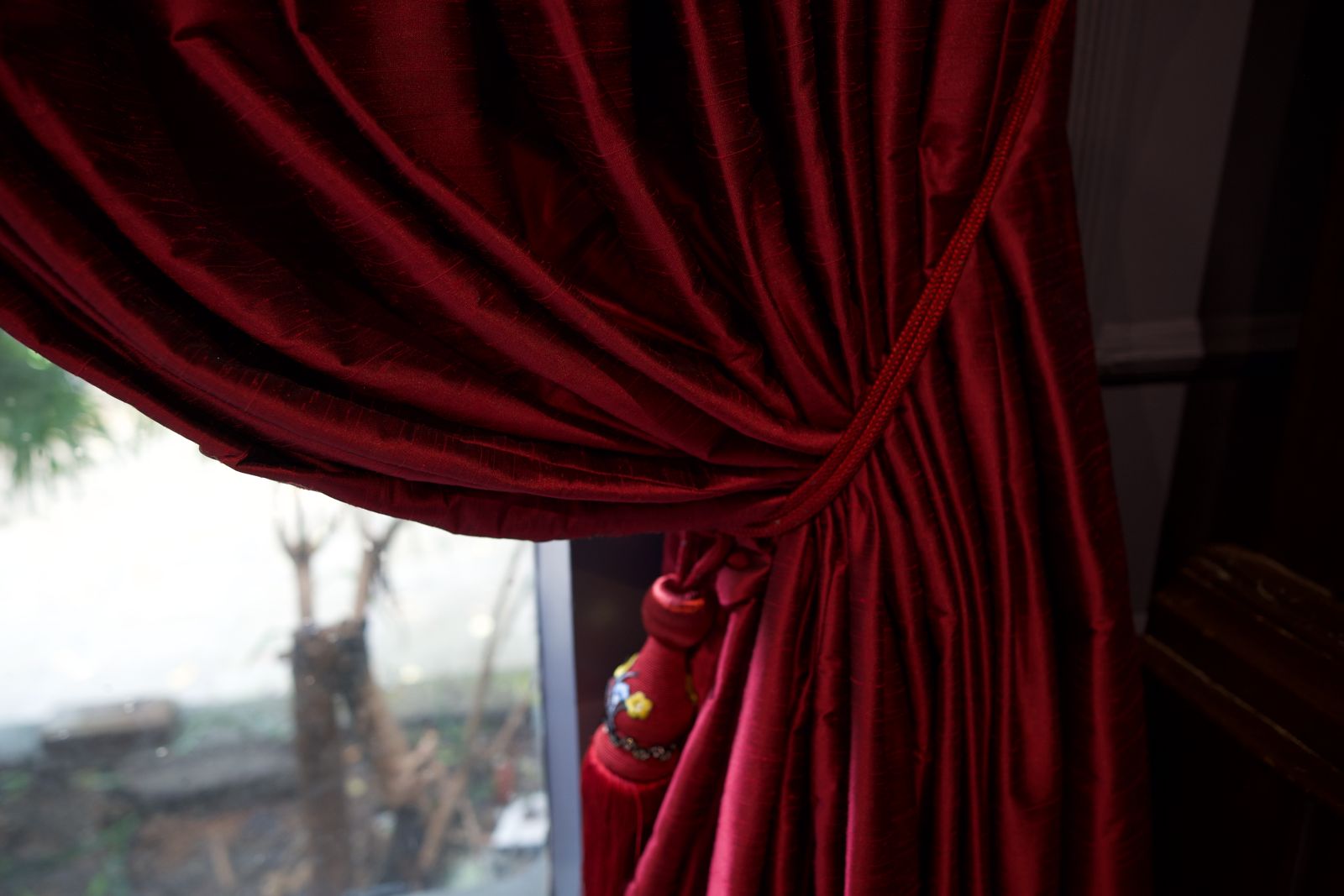 Close-up of deep red drapery panels gathered beside a window.