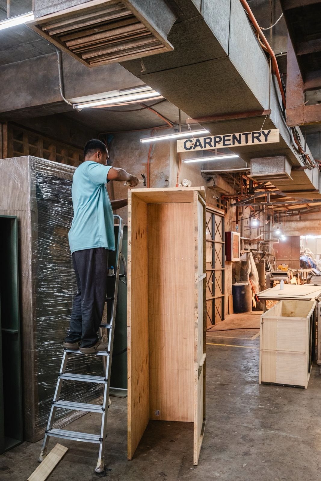Danilyns craftsperson building a tall wooden cabinet beneath the Carpentry sign in the workroom